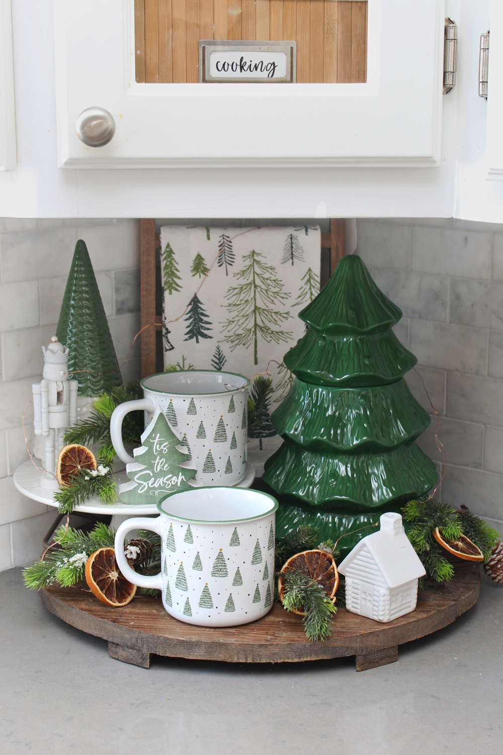 Wooden kitchen tray decorated with green and white Christmas tree decor.